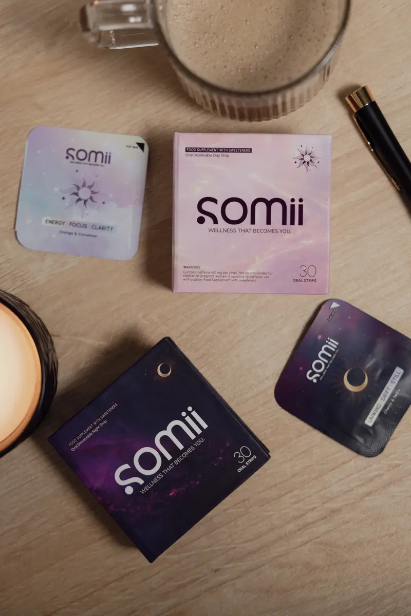 Somii boxes and strip sachets laid out on a wooden desk beside a coffee and a candle